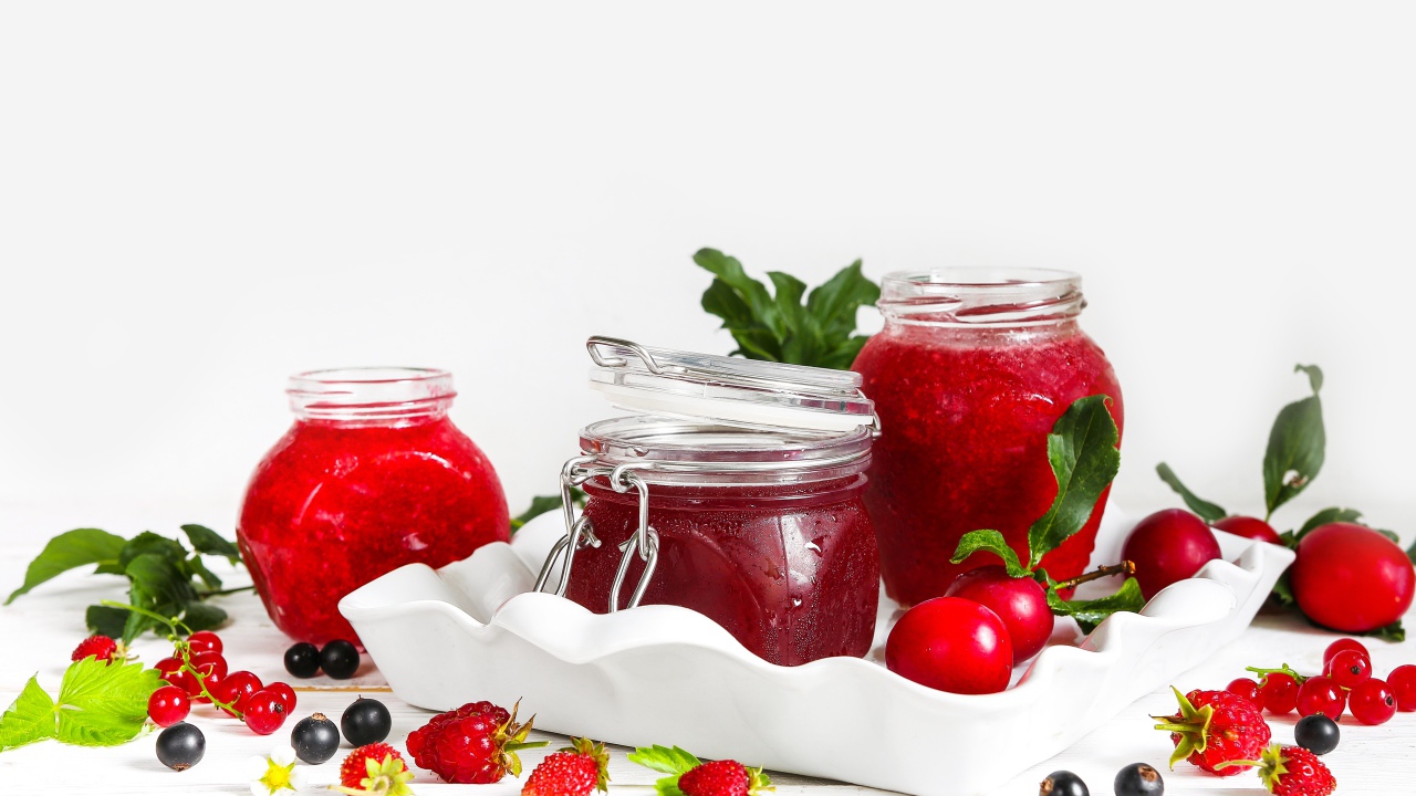 Три банки джема с ягодами на белом фоне