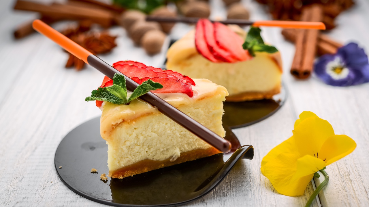 Два куска чизкейка с клубникой на столе с палочками