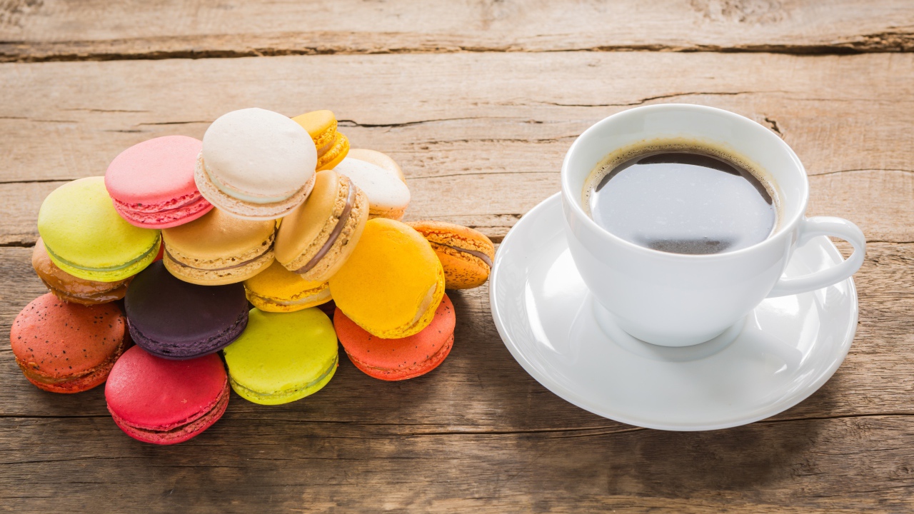 Белая чашка кофе на столе с разноцветным десертом макарун