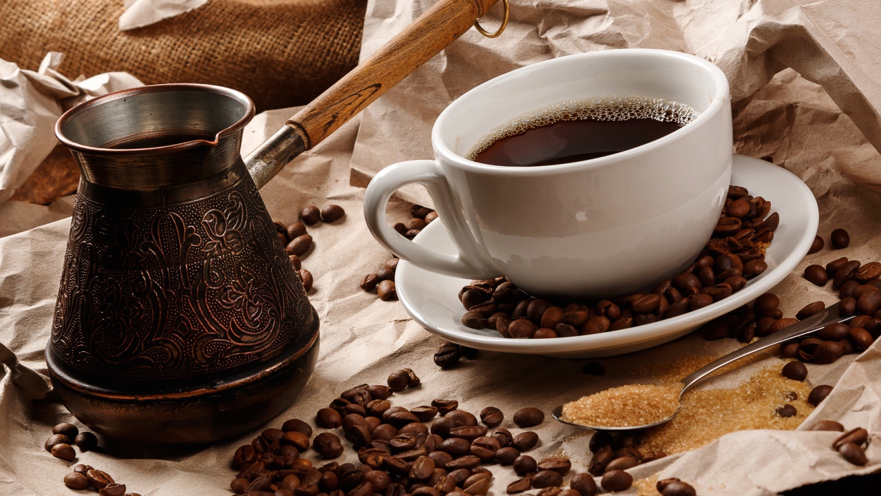 Чашка горячего кофе на столе с туркой, зернами и коричневым сахаром