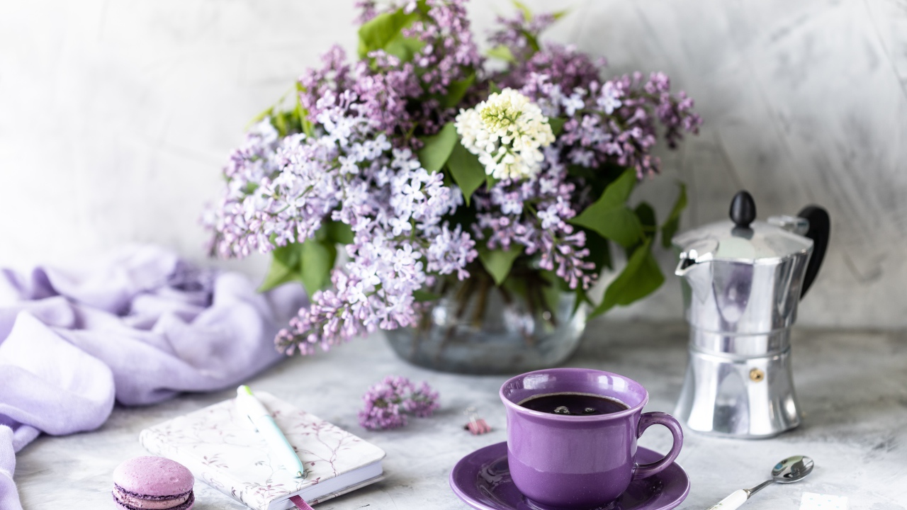 Cup of coffee on a table with a notebook and a bouquet of lilacs in a vase