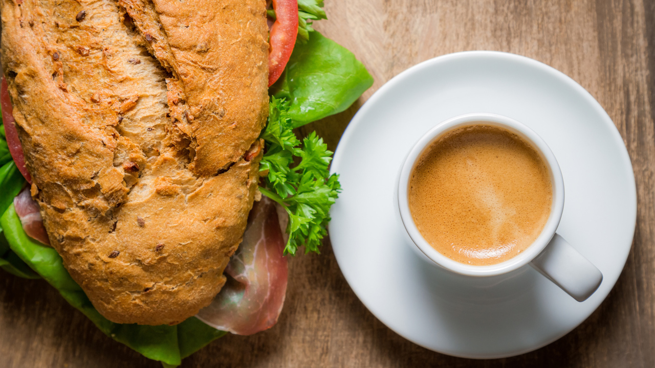 Чашка кофе с бутербродом на столе к завтраку 