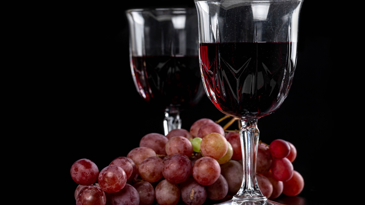 Два бокала вина на черном фоне с виноградом 
