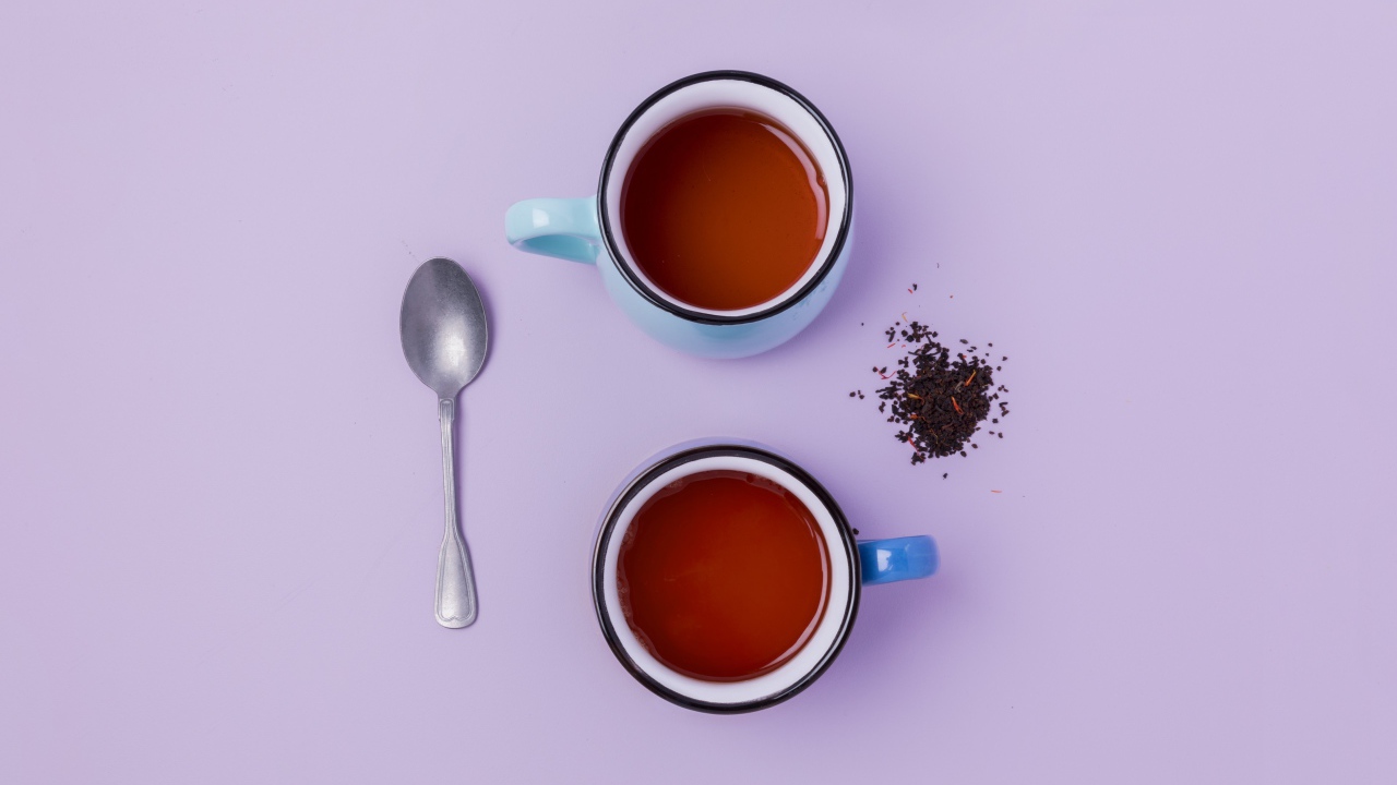 Две железные чашки чая на сиреневом фоне с ложкой
