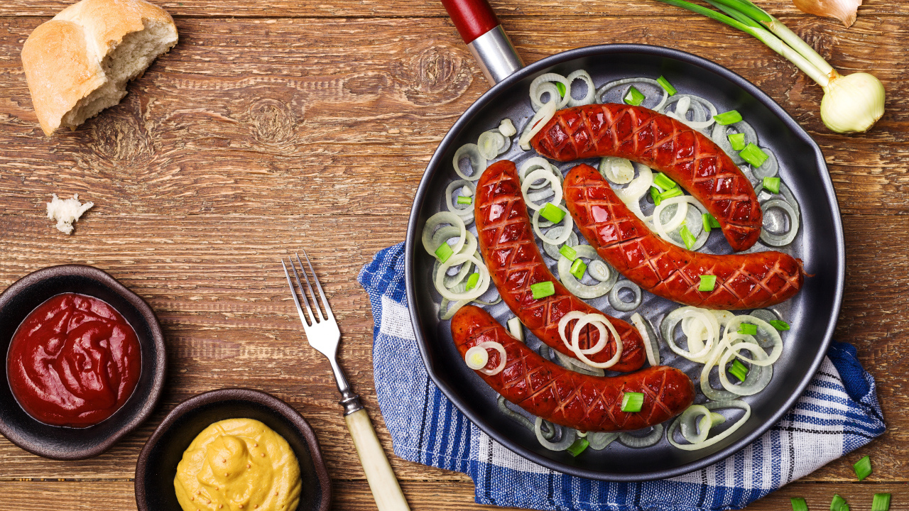 Колбаски барбекю с луком на сковороде на столе с соусом