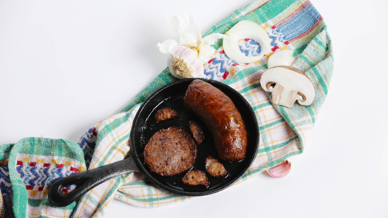 Сковорода с жареной колбасой на столе с полотенцем и чесноком