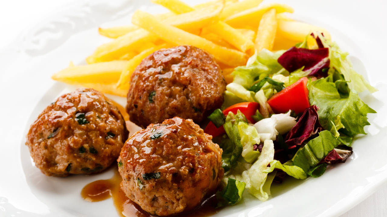 Фрикадельки с салатом и картофелем фри на белой тарелке