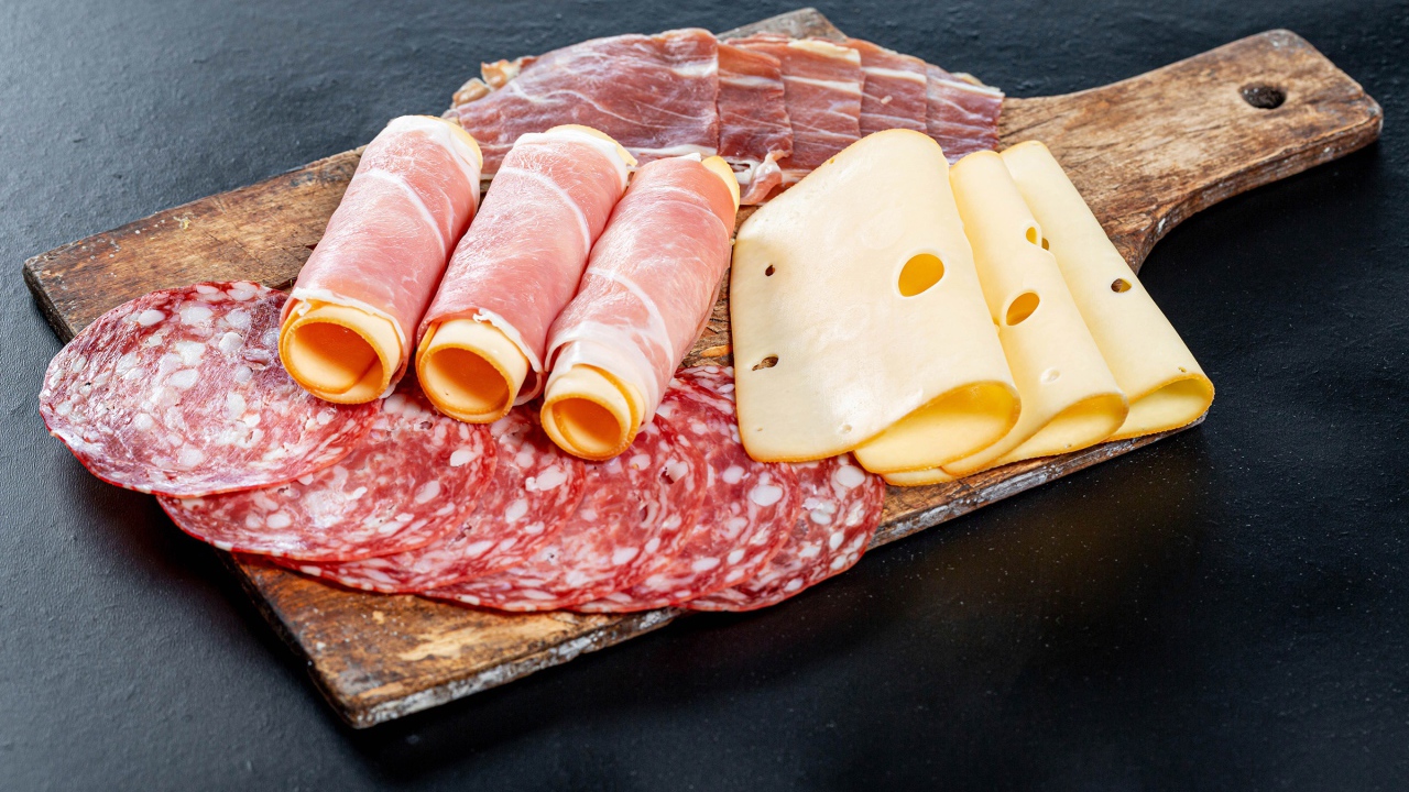 Куски сыра, ветчины и колбасы на доске