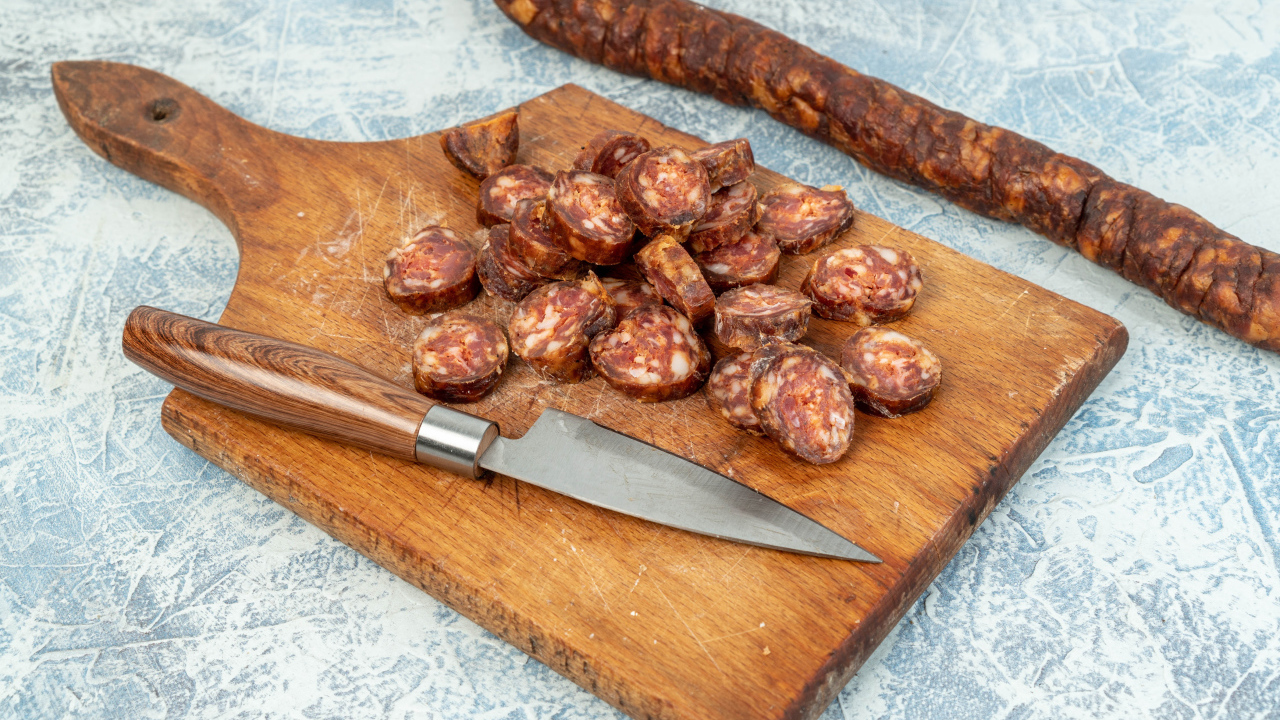 Колбаса нарезана колечками на разделочной доске с ножом 