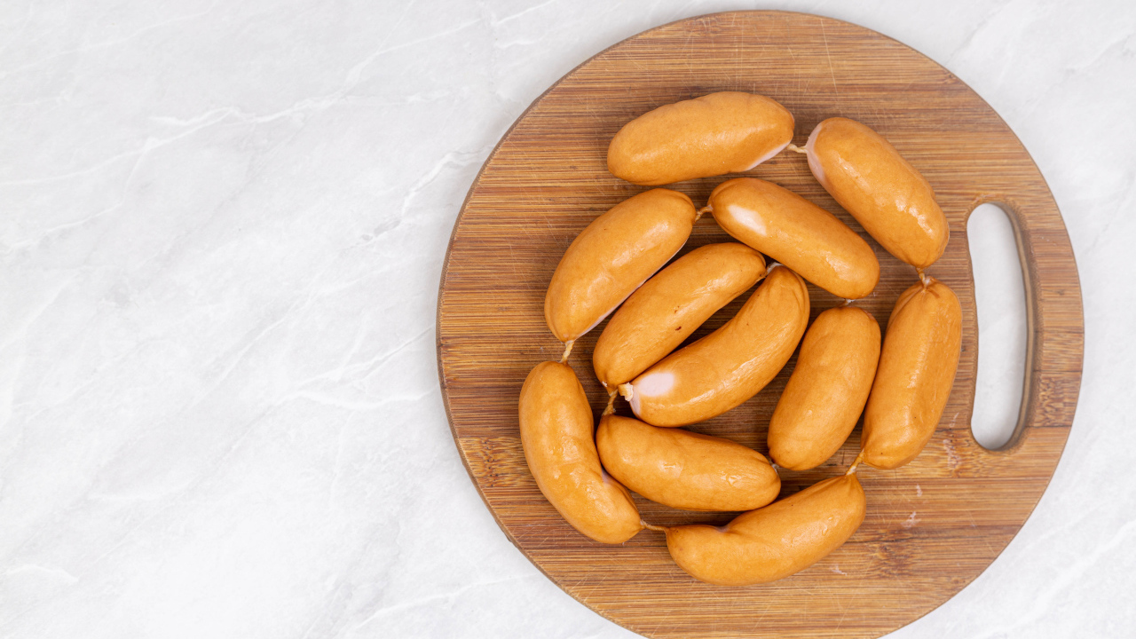 Копченые сардельки на деревянной доске на сером фоне