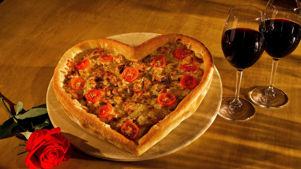 Heart-shaped pizza on a table with a rose and two glasses of wine