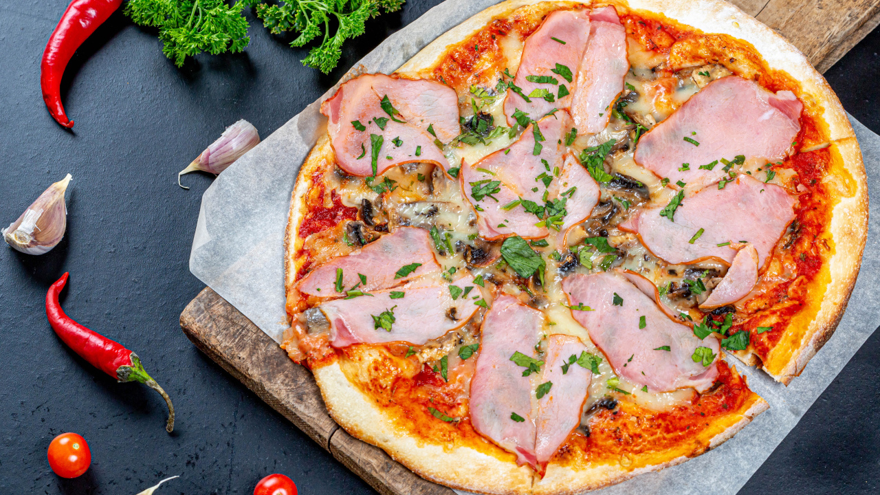 Large pizza with ham on a table with pepper, garlic and parsley