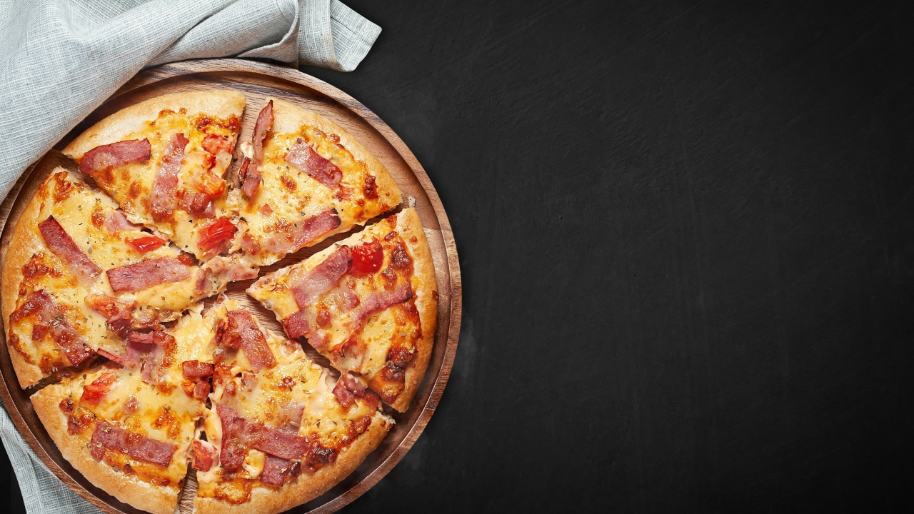 Пицца с кусочками бекона на доске на черном фоне