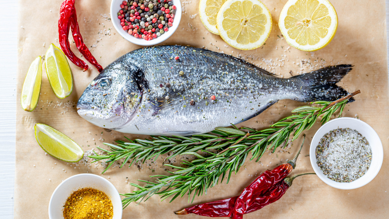 Свежая рыба на столе со специями, лимоном, розмарином и красным перцем