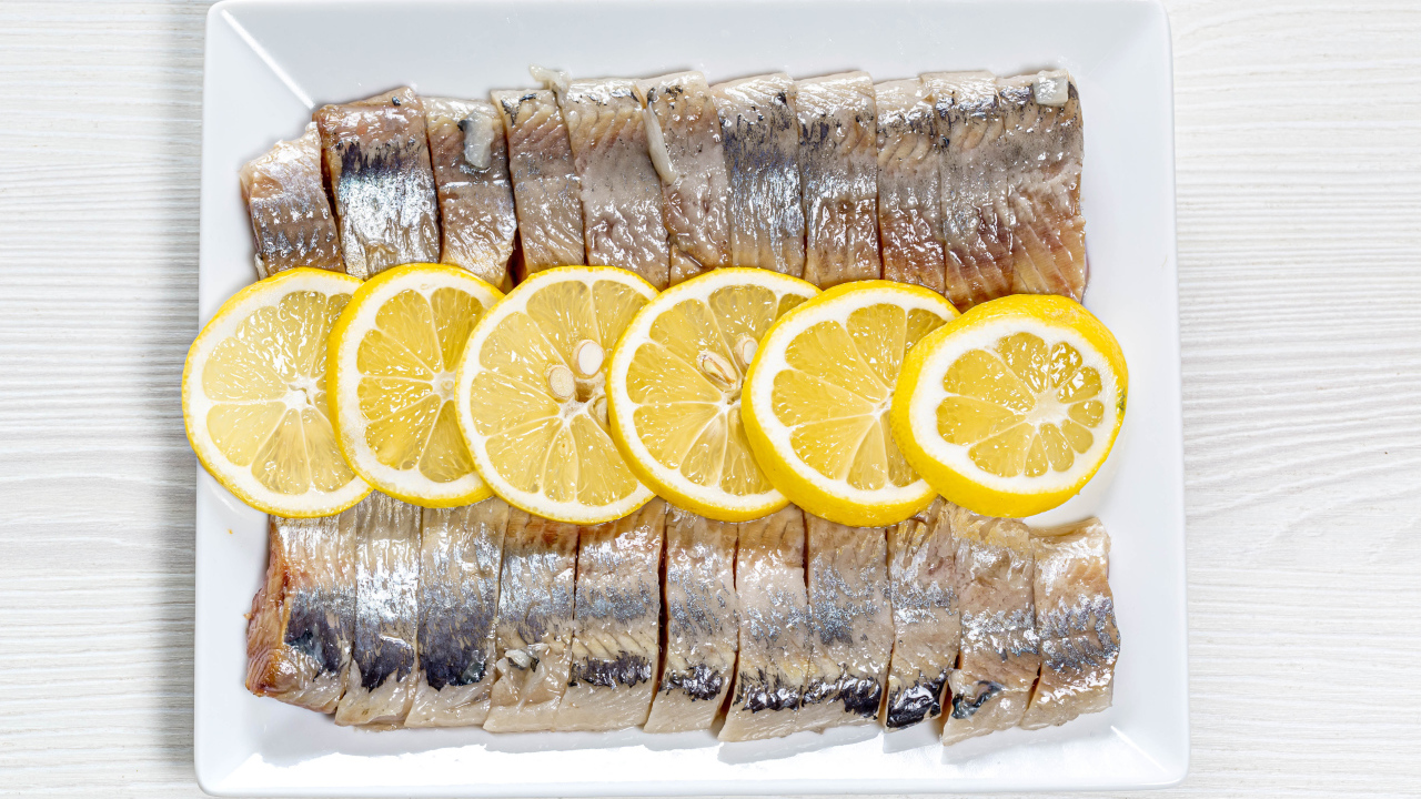 Селедка нарезанная кусочками на белой тарелке с лимоном 