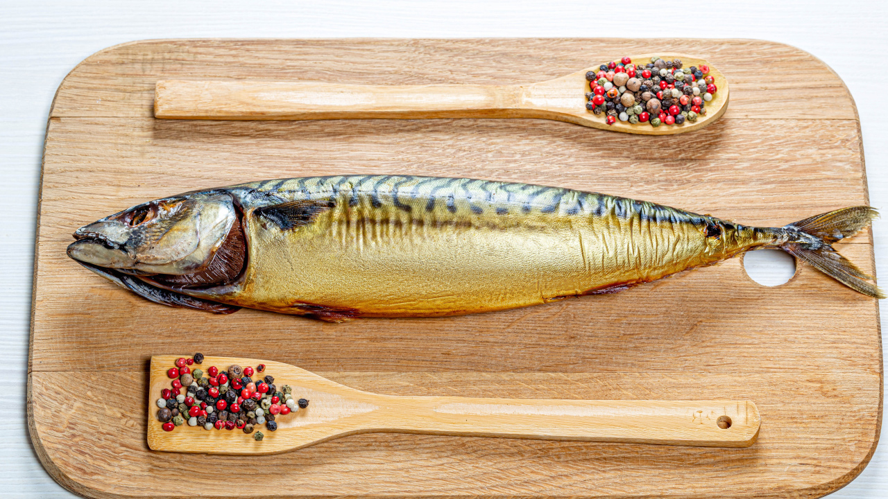 Копченая скумбрия на разделочной доске с перцем на белом фоне
