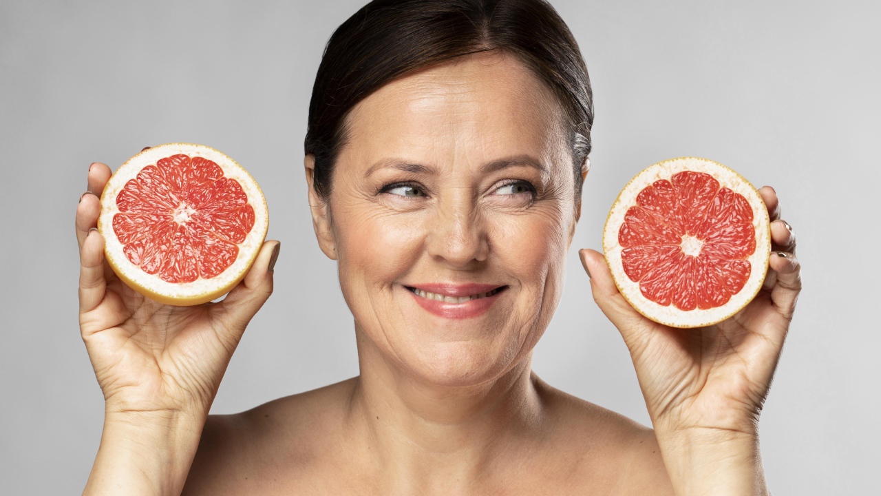 Улыбающаяся женщина с грепфрутом в руках на сером фоне