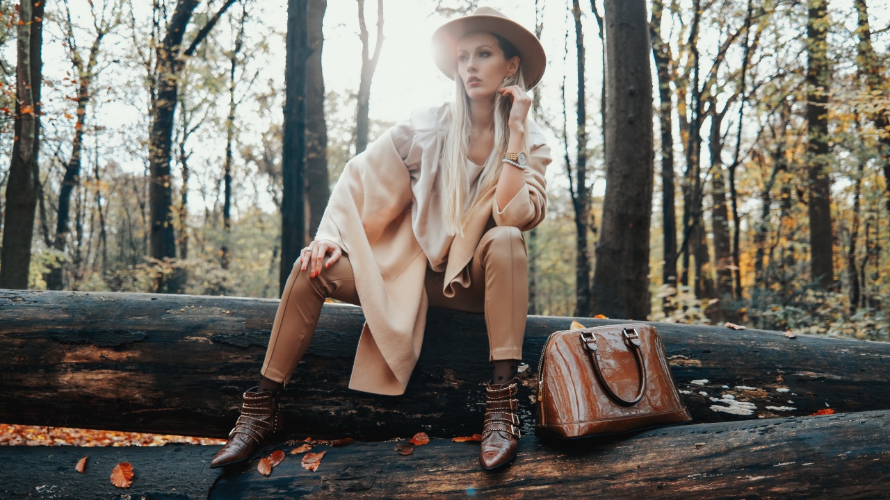 Девушка в пальто сидит на упавшем дереве в лесу 