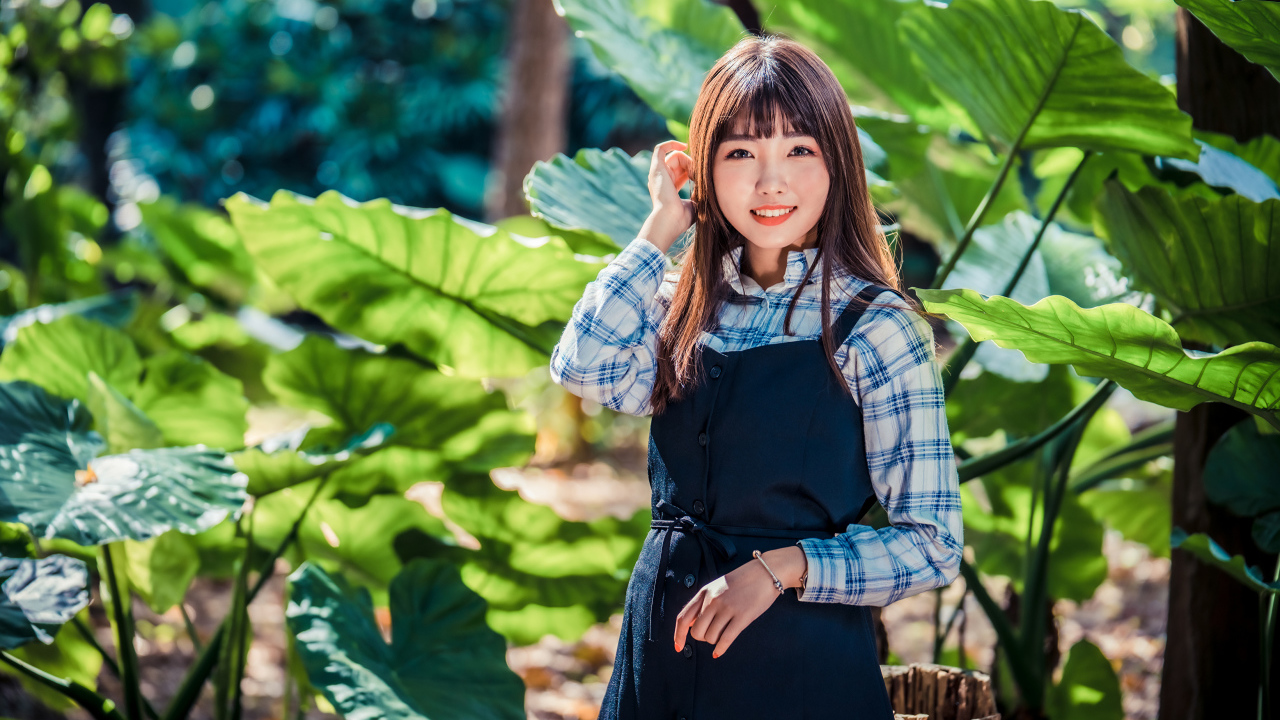 Улыбающаяся девушка азиатка в черном платье стоит в парке