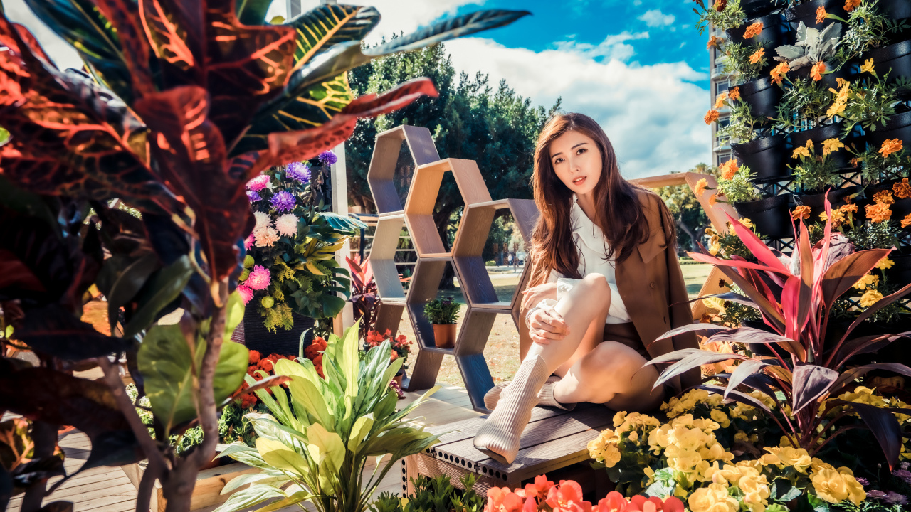 Молодая азиатка сидит возле клумбы с цветами