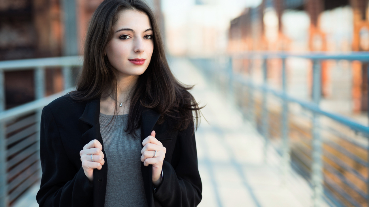 Молодая девушка в черном пальто стоит на мосту