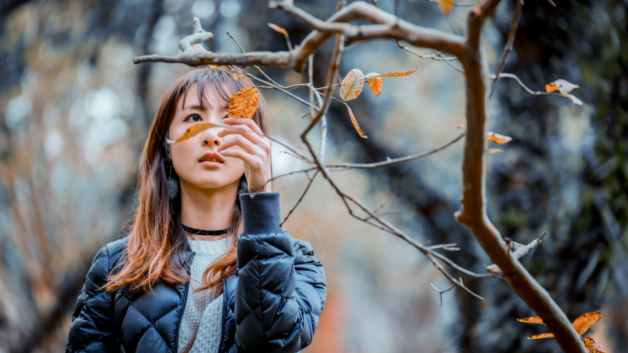 Девушка азиатка в черной куртке у дерева