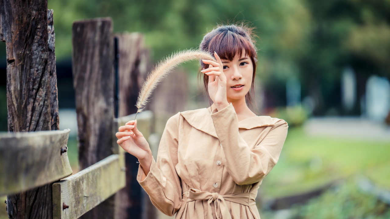 Девушка азиатка в пальто стоит у забора 