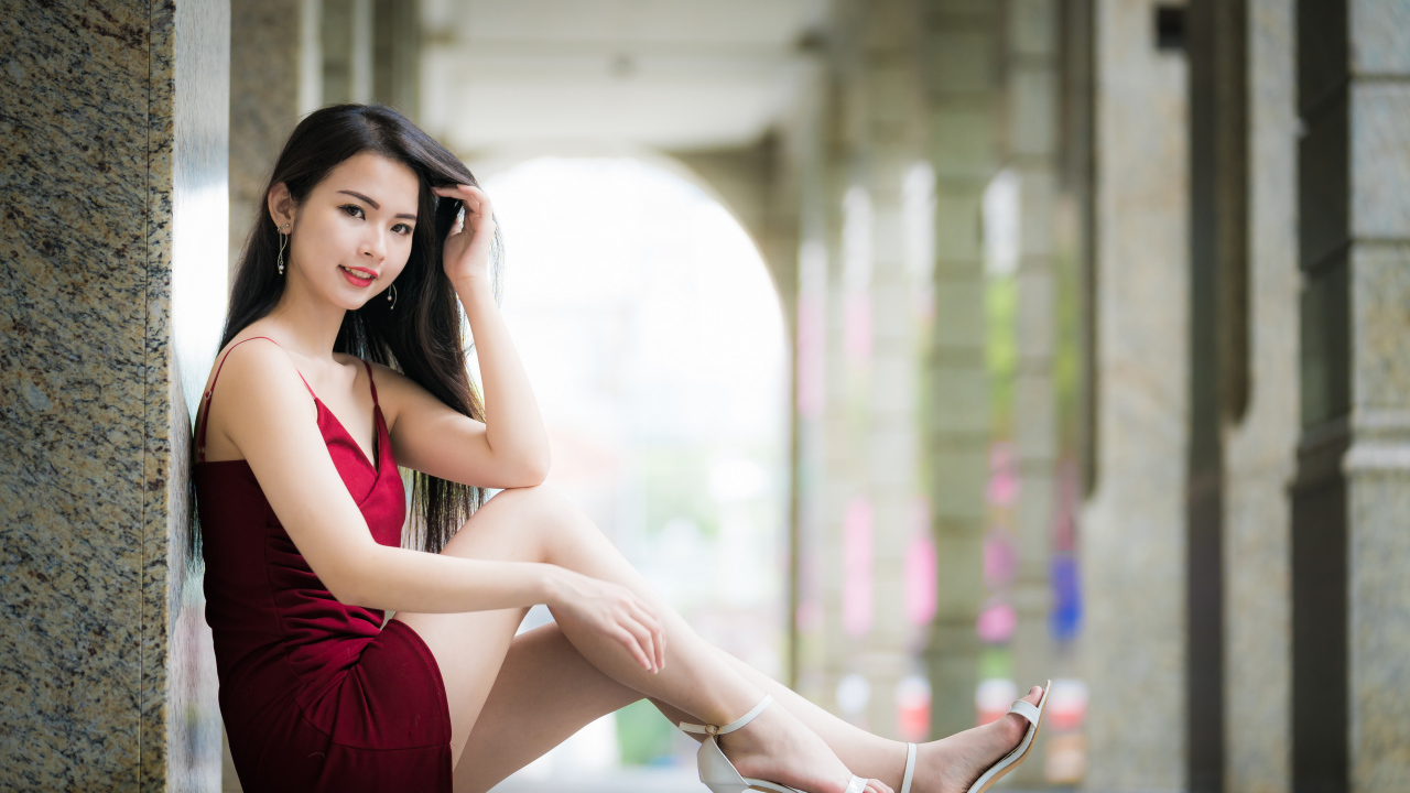 Девушка азиатка в красном платье сидит на полу