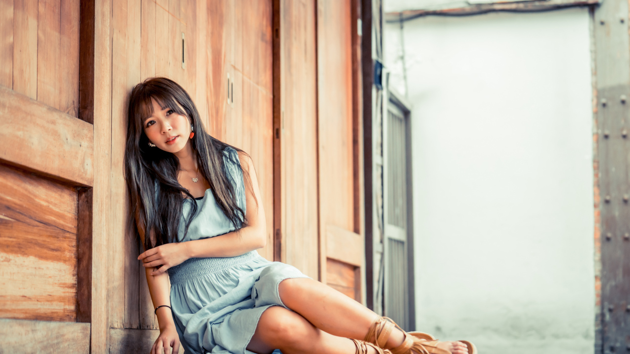 Девушка азиатка в платье сидит на полу у стены 