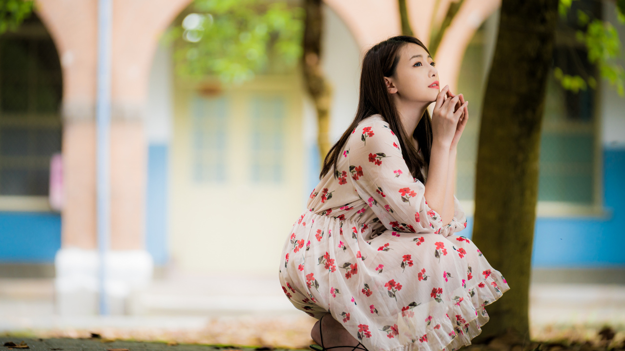 Красивая девушка азиатка в платье сидит под деревом в парке