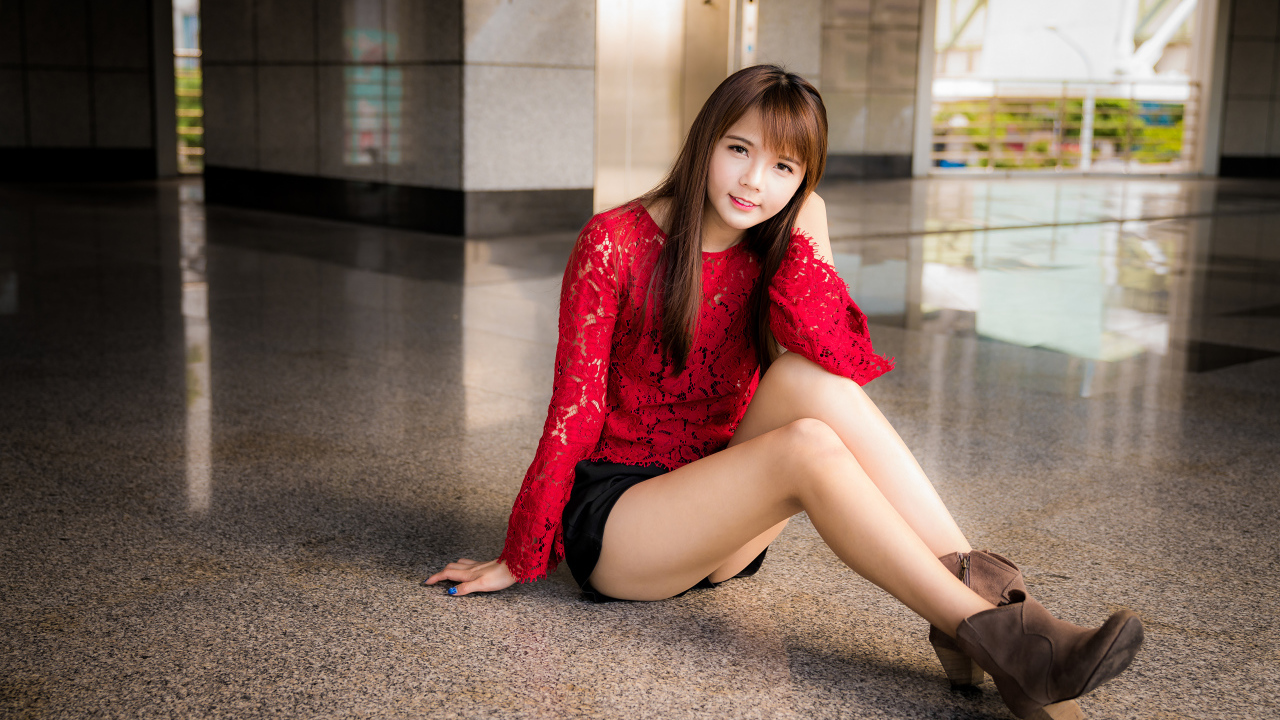 Красивая девушка азиатка в красной блузке сидит на полу
