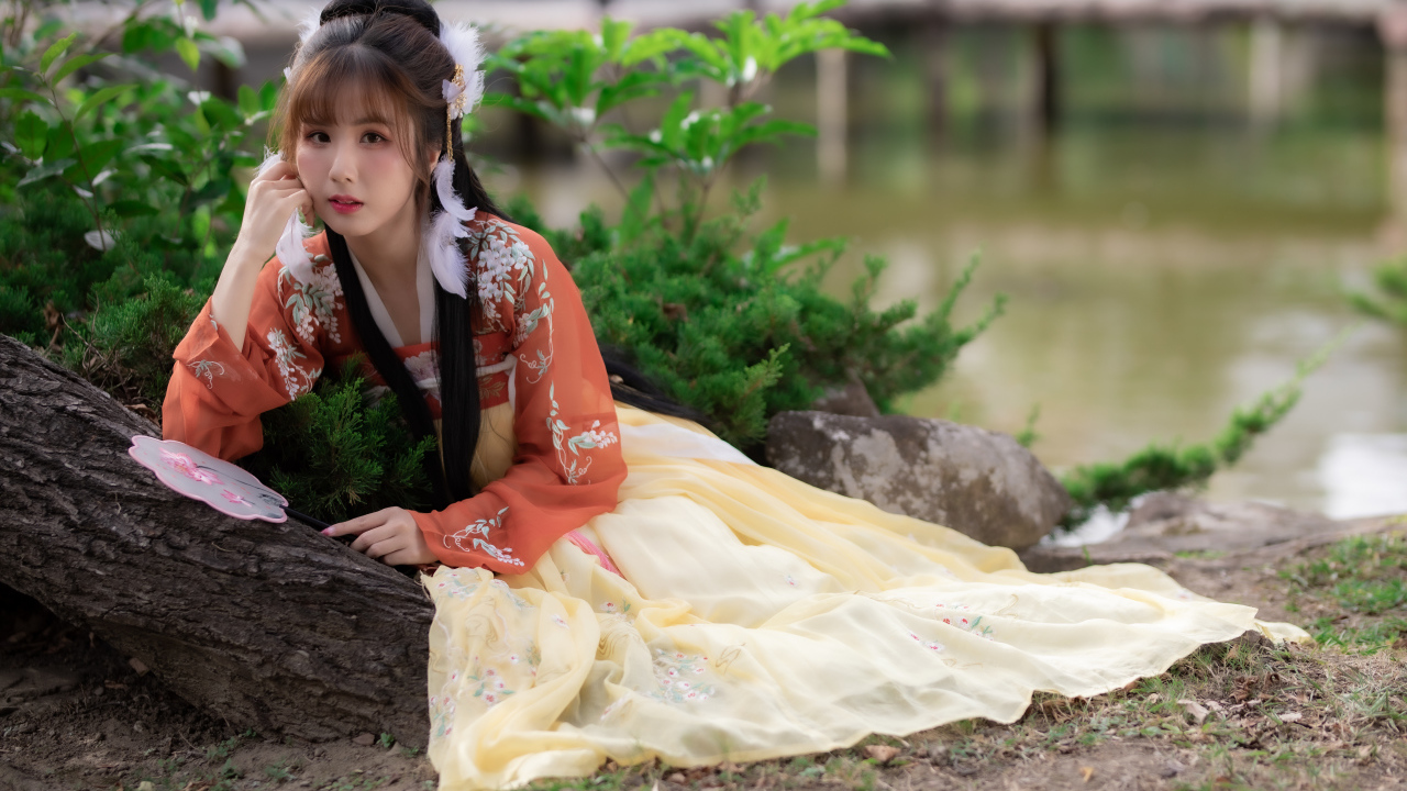 Красивая девушка азиатка сидит на земле у дерева 