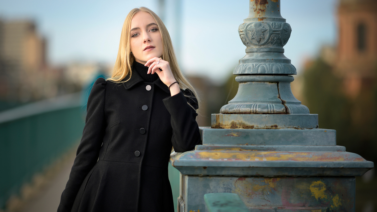 Красивая блондинка в черном пальто стоит у фонаря