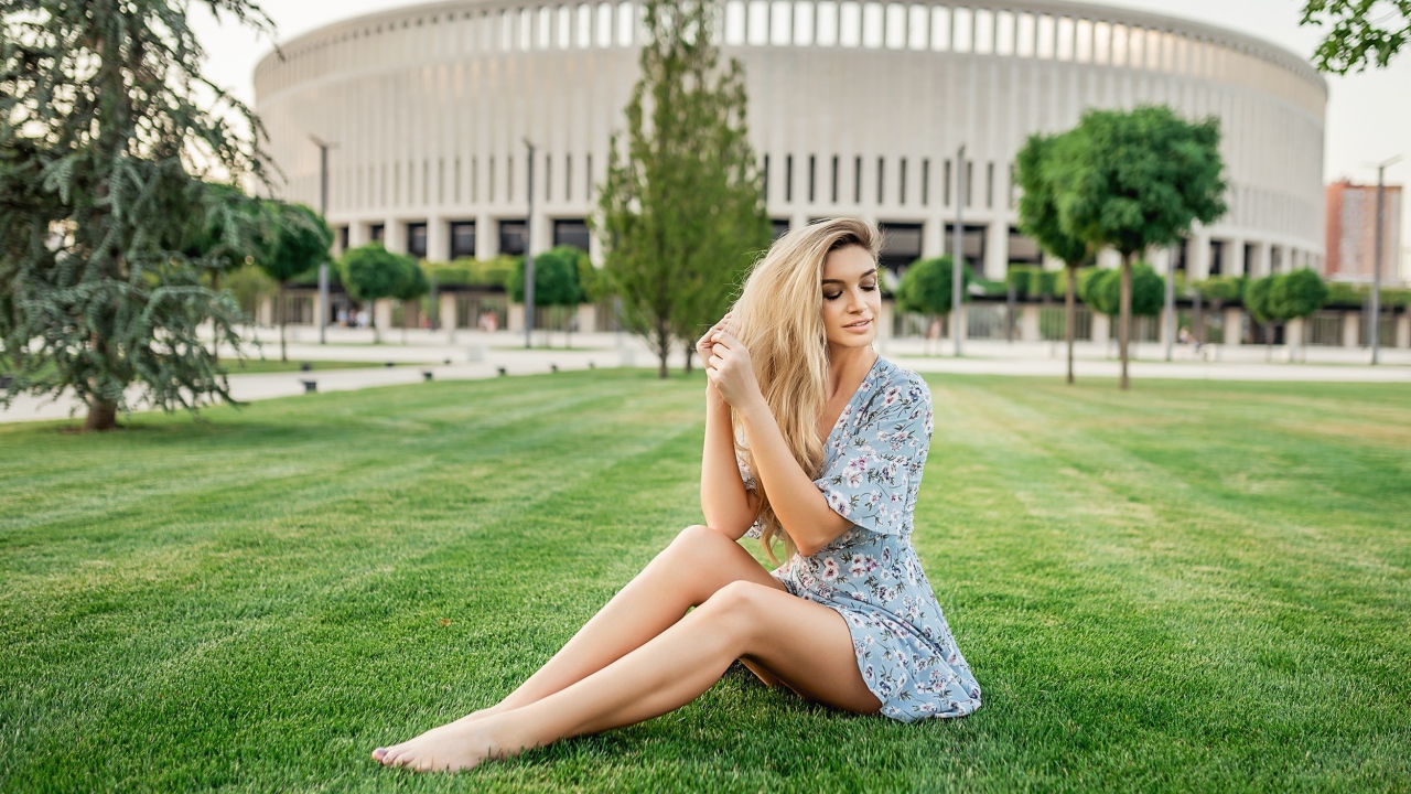 Красивая девушка в платье сидит на зеленом газоне 