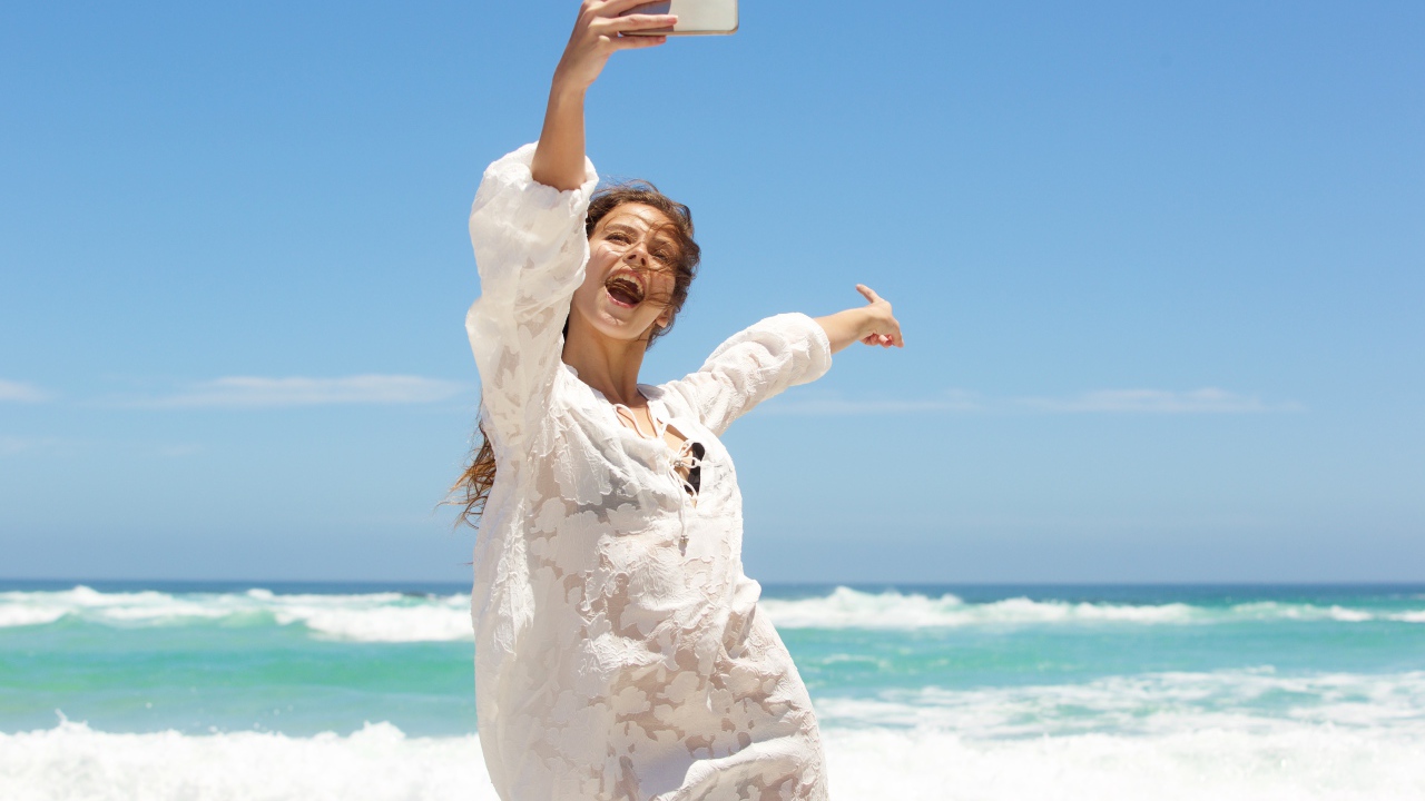 Красивая девушка в белом платье делает селфи на море 