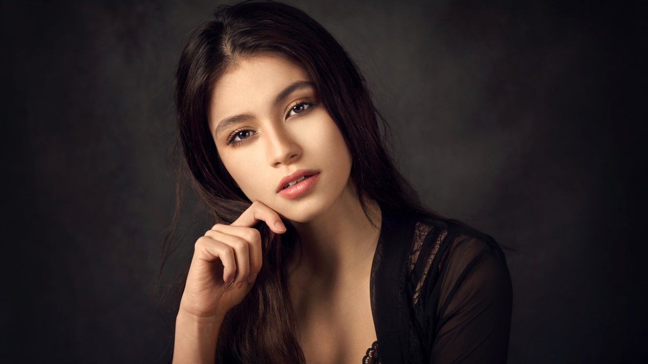 Красивая девушка в черном сидит на сером фоне