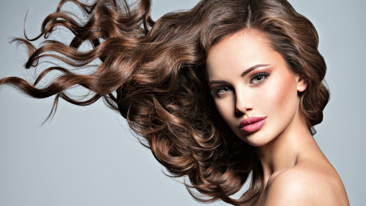 Красивая девушка модель с волнистыми волосами на сером фоне