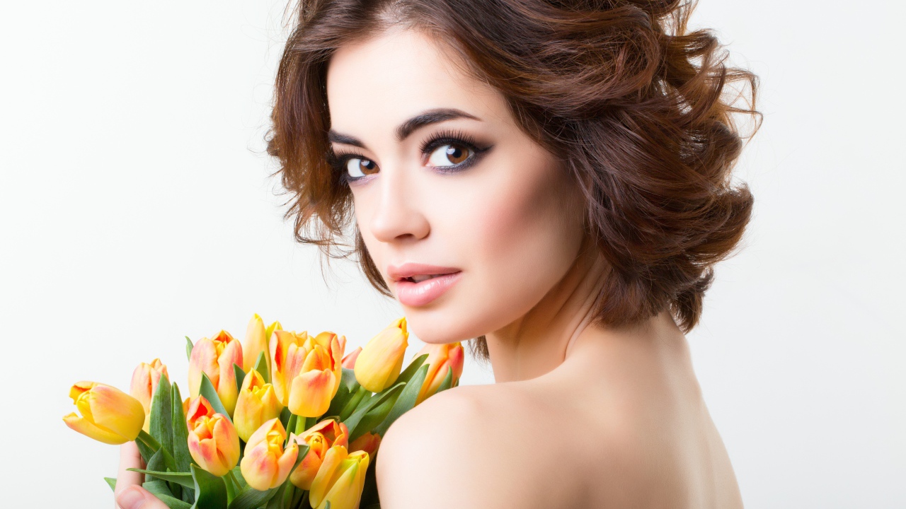 Красивая девушка с прической в букетом тюльпанов в руках на белом фоне