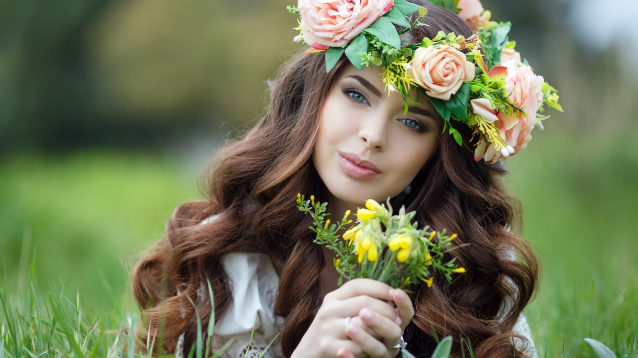 Красивая девушка с венком на голове лежит на зеленой траве