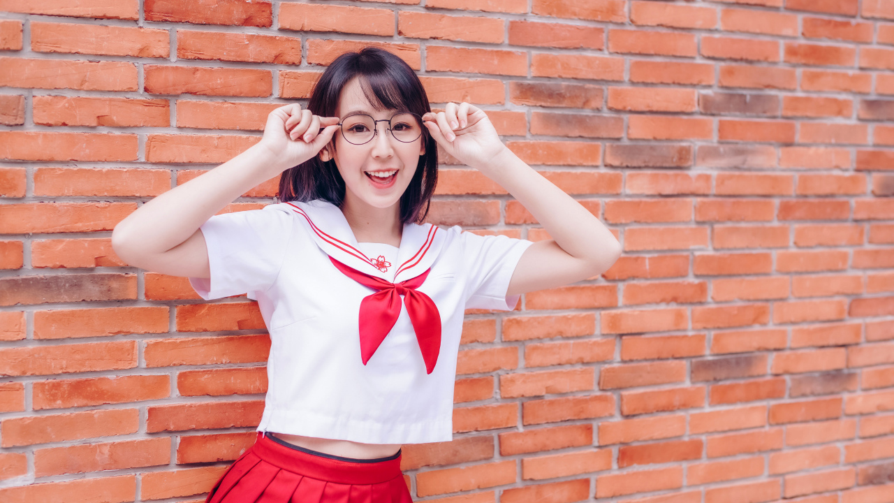 Яркая веселая азиатка в очках у кирпичной стены