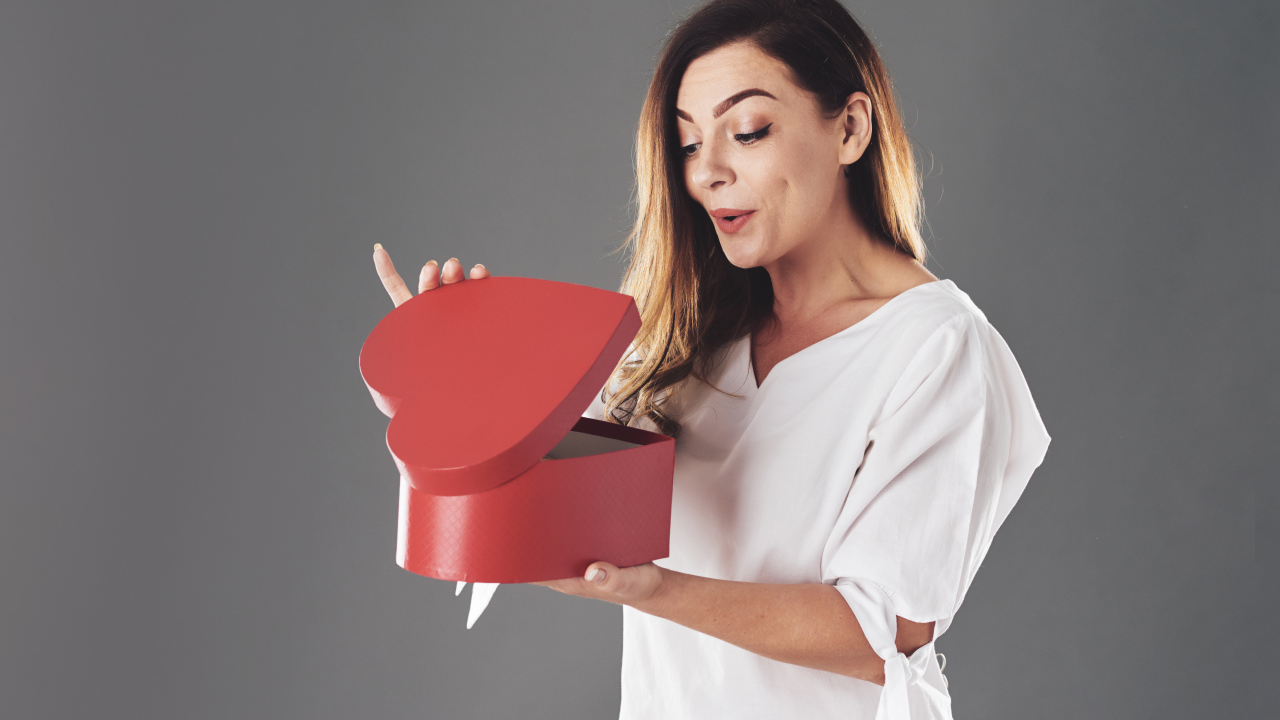 Любопытная девушка смотрит в красную коробку в форме сердца