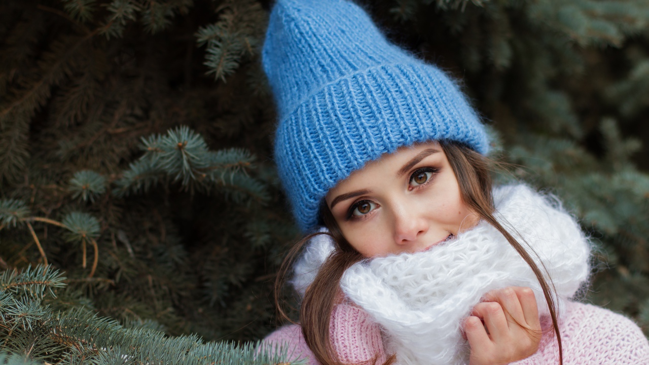 Девушка в голубой вязаной шапке у ели