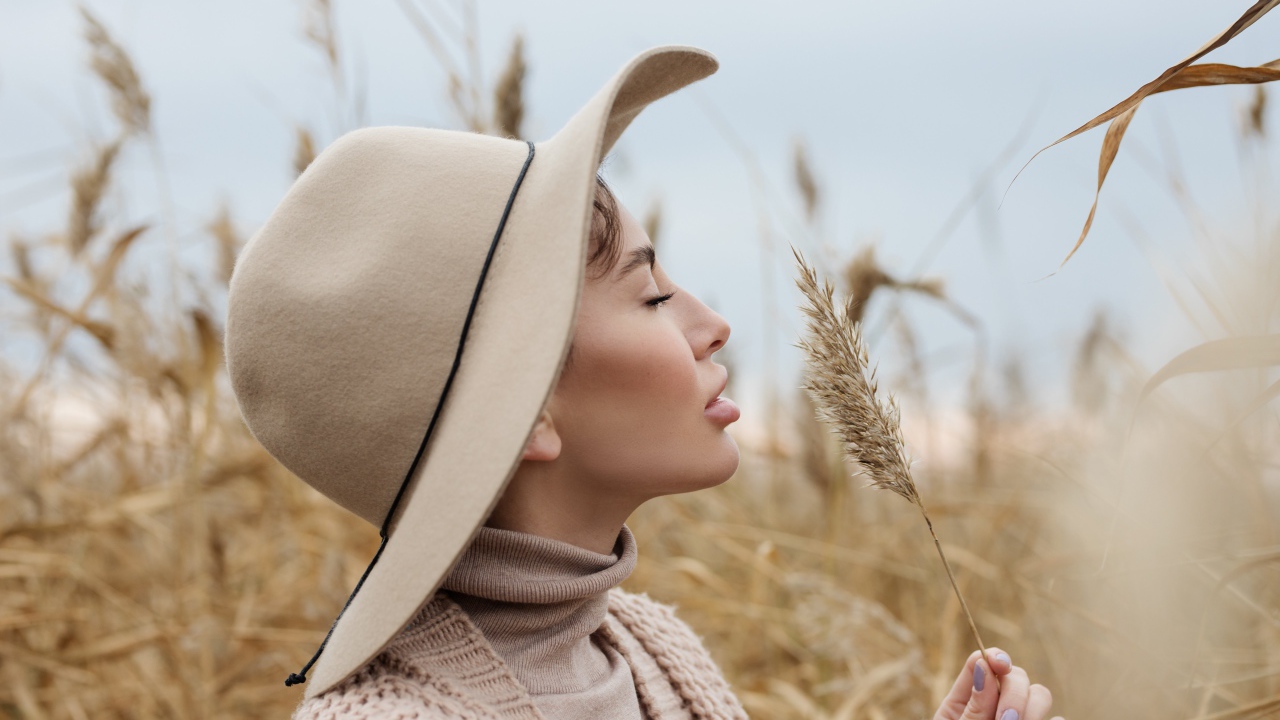 Девушка в шляпе с закрытыми глазами держит колосок 