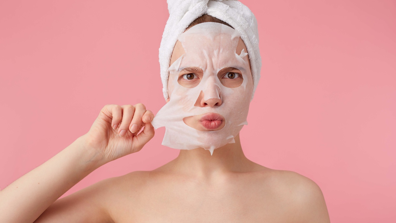 Девушка снимает косметическую маску с лица на розовом фоне 