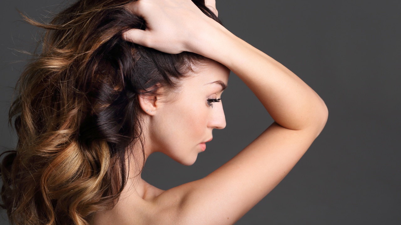 Девушка с руками в волосах на сером фоне