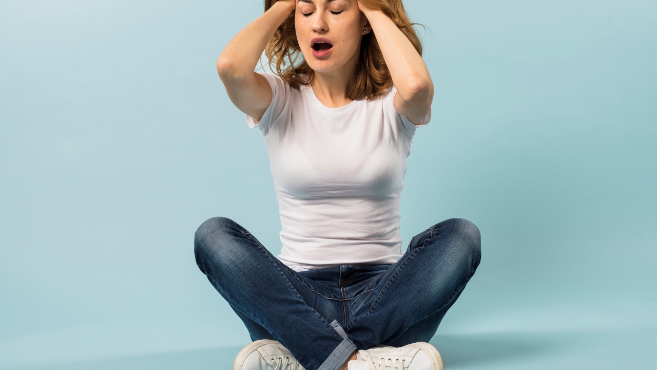 Девушка с руками в волосах сидит в джинсах на голубом фоне