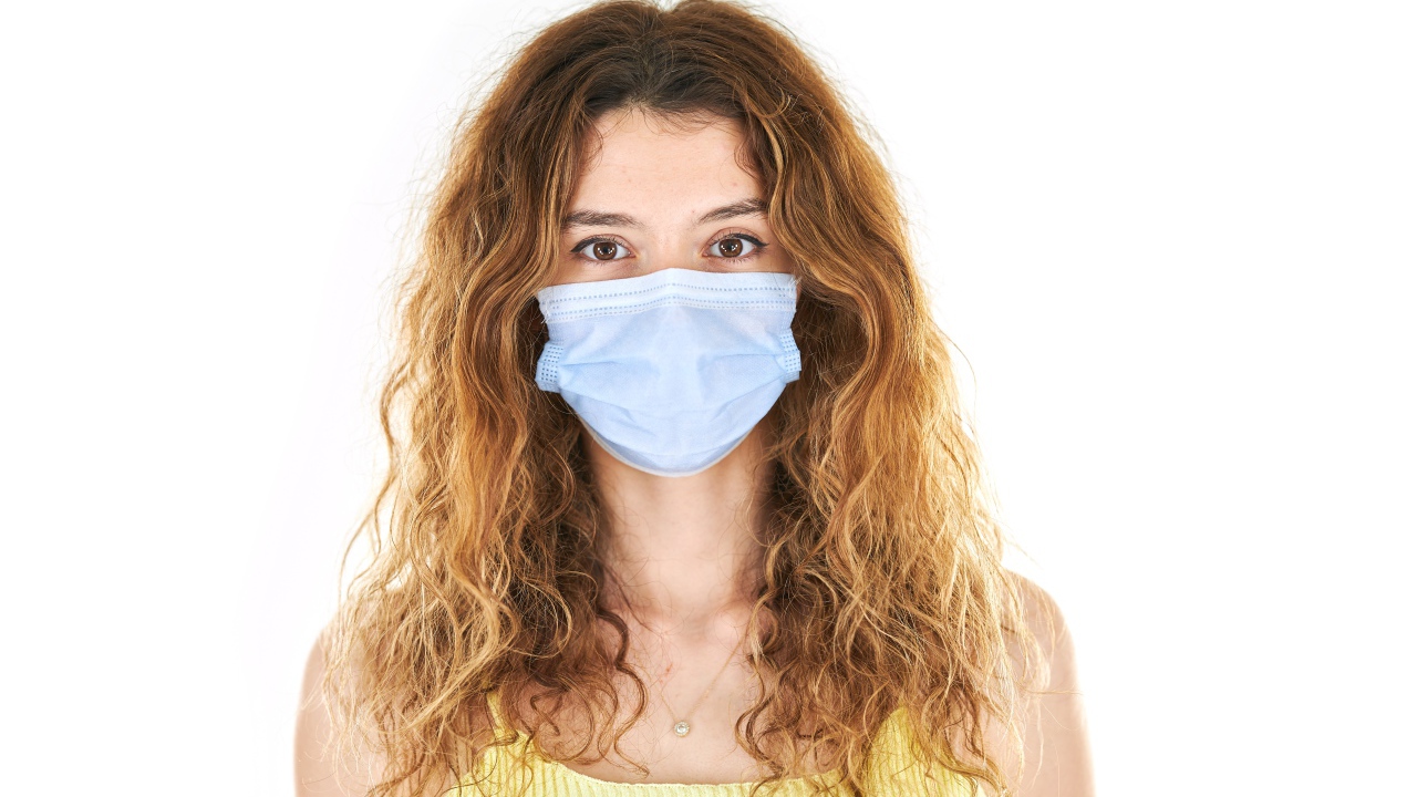 Длинноволосая девушка в маске от коронавируса на белом фоне