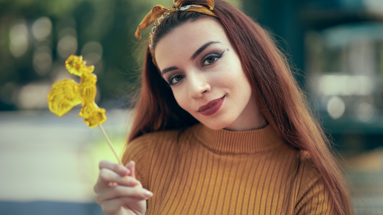 Длинноволосая девушка в свитере с леденцом в руке