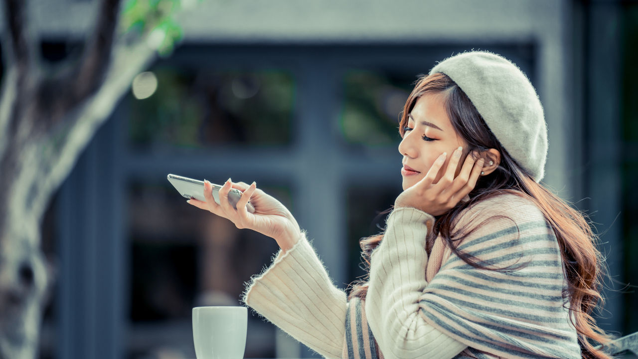 Мечтательная девушка с телефоном сидит в кафе 