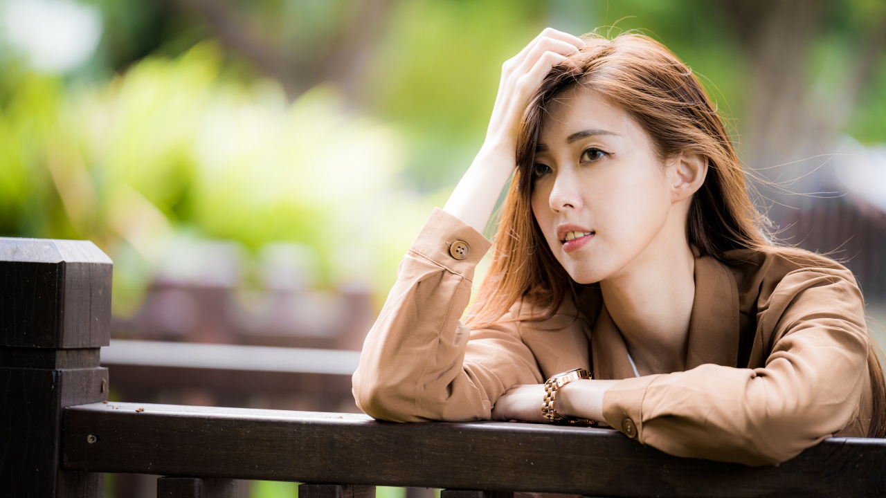 Грустная девушка азиатка стоит у деревянных перил 